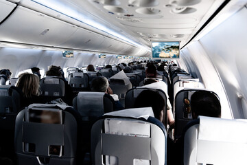 Fototapeta premium Passenger cabin of commercial aircraft with unrecohnizable travellers seated on their seats during flight.
