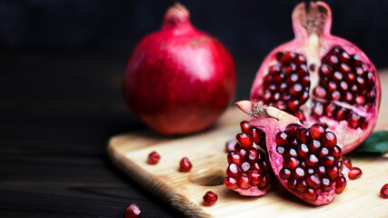 Ripe pomegranate fruit near leaf on dark wooden background