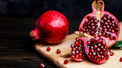 Fototapeta na wymiar Ripe pomegranate fruit near leaf on dark wooden background