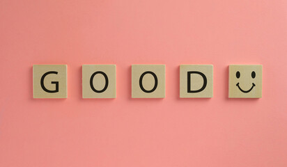 Good word and smile icon on wooden cube over pink pastel background.