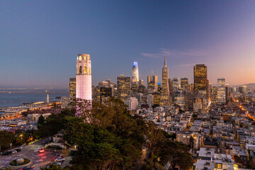 Fototapeta premium Nighttime aerial view of the San Francisco skyline with Coit Tower prominent in the frame. Bay Bridge in the background.