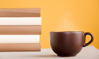 Brown cup of coffee or tea with hot steam, on the table, with books
