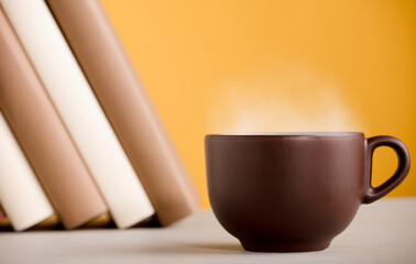 Brown cup of coffee or tea with hot steam, on the table, with books