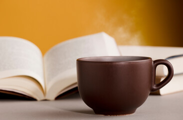 desk with cup of coffee or tea with hot steam , open books, orange yellow background