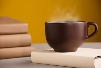 Brown cup of coffee or tea with hot steam, on the table, with books
