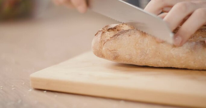 Female cut slice baguette bread knife in hands kitchen board close up