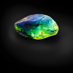 A parti coloured rough sapphire gemstone on black background