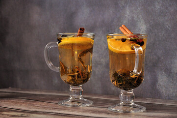 Two glasses of herbal tea with spices and a slice of lemon are on a wooden table.