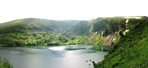 A panoramic shot of an alpine lake lying in a deep hollow with negams on the slopes.