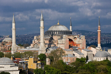 Fototapeta na wymiar Istanbul, Turkey: Minarets of a local mosque and the orange-walled Hagia Sophia Museum rise into a cloudy sky above Hagia Eirene at Topkapi Palace Museum.