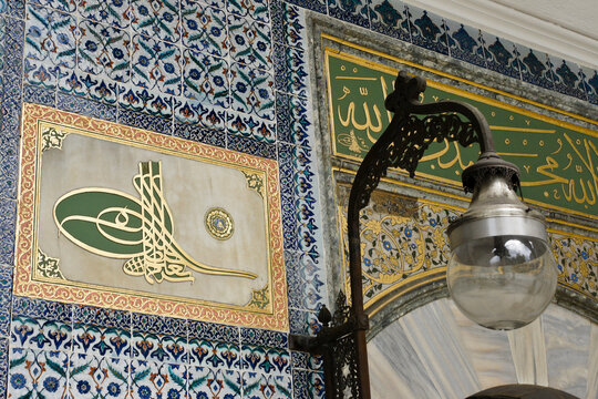 Istanbul, Turkey: A calligraphic monogram (tughra) of an Ottoman sultan is surrounded by blue and white Iznik tilework next to a lamp at Topkapi Palace, a UNESCO World Heritage Site.