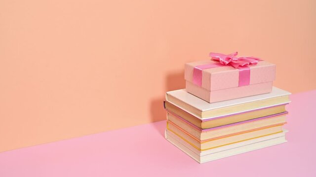 Pastel pink gift with bow appear on stack of hardcover books on bright pink orange theme. Stop motion