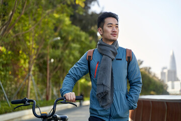 asian young man walking with bicycle in park