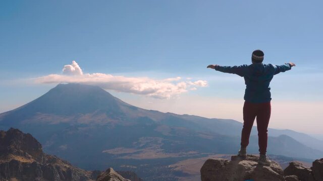 Young man standing on the edge of a cliff on top of the iztaccihuatl volcano with magnificent views of the popocatepetl volcano.