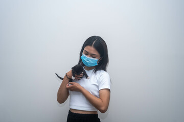 Young girl wearing face mask carrying a baby kitten with tuxedo black and white pattern