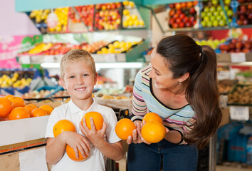 Fototapeta premium .Little child with his mother choosing fresh oranges at fruit department of supermarket