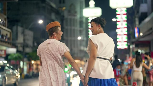 Asian lgbtq guy friends wearing woman clothes meeting together in the city with crowd people walking down street at night. Diversity sexual equality, lgbtq pride and transgender cross-dressing concept