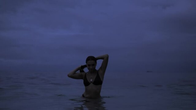 Beautiful girl coming out of the ocean and enjoy twilight light on purple sky