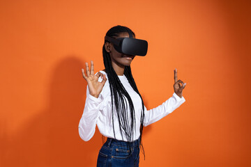 3d technology, virtual reality, entertainment, cyberspace and people concept - young african-american girl in vr-glasses showing the okey sign with both hands on orange background with copy space