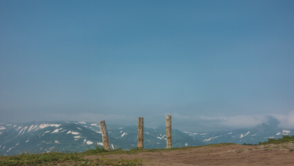 Old wooden carved totem poles stand on the hill. In the distance you can see a mountain range with...