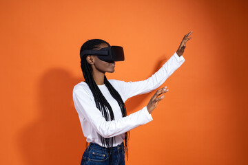 A young African-American woman wearing vr glasses sees something and tries to touch it with her...