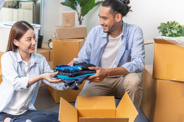 Attractive young Asian couple preparing old used clothes and put into the box for donate or sharing to another people. Product recycle or volunteer sharing donation concept.	