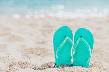 Fototapeta na wymiar Turquoise or light blue flip flops or sandal shoe stuck in the sand on sandy beach by the sea coastline or ocean. Travel or vacation concept in hot countries in summer or winter. High quality photo