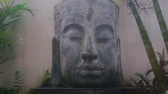 Peaceful rainy scape of large concrete Buddha head sculpture in Asian jungles, place for mindfulness meditation, religion and historical landmark