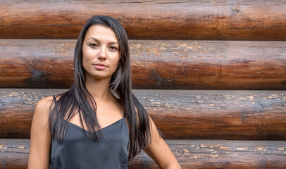 Portrait of a beautiful brunette on the background of a log house