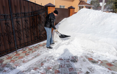 a man cleans snow with a shovel in the yard in winter