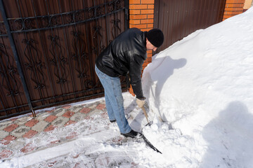 Naklejka na ściany i meble a man cleans snow with a shovel in the yard in winter