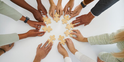 Multiethnic team of young business people connecting pieces of jigsaw puzzle on white table. Human...