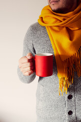 A man with a red mug of coffee in his hand wearing a cardigan and scarf. The concept of autumn. Front view.