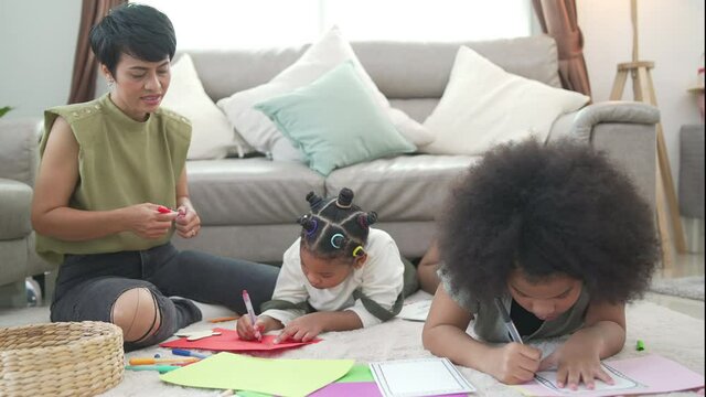 4K African family parent and two little daughter sitting on the floor using color pencil painting and drawing on paper book together. Mom with child girl kid enjoy and having fun homeschooling at home