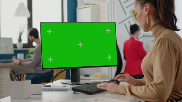 Company worker using isolated green screen on monitor with chroma key. Business woman looking at computer with mock up template and background in startup office. Mock-up copy space