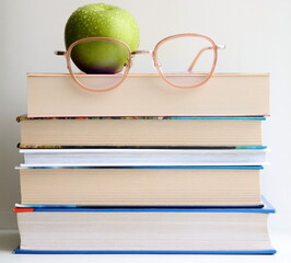 Stack of books on table, on white background. Green apple and glasses.