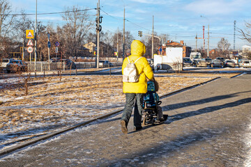 Mom rides her daughter on a sleigh on the sidewalk on a sunny winter day