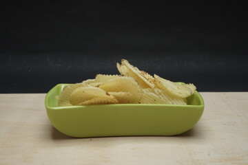 Salted Potato Wafers in Green Square Bowl on Wooden Table, Heap of Wafers, Copy Space, Heap of Chips, Side View, Isolated In Black Background