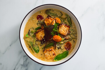 vegan thai green curry with pan fried silken tofu and freshly picked vegetables, healthy plant-based food