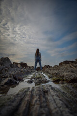 Obraz premium girl in denim overalls, looking towards the sea on some stones