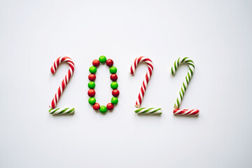 Year 2022 laid out from round multicolored candies and striped candy canes on white background