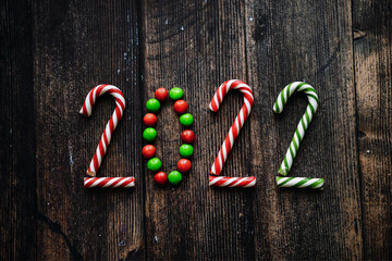 Year 2022 laid out from round multicolored candies and candy canes on wooden background