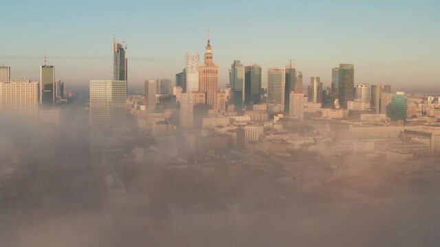 Amazing shot of downtown panorama coming out from dense fog. Group of high rise buildings lit by morning sun. Warsaw, Poland