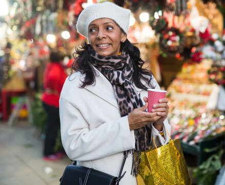 Happy woman holding hot cup of coffee in hands at street christmas fair