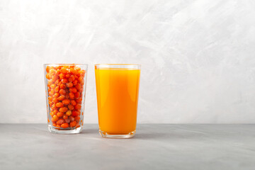 Natural sea buckthorn juice and  Frozen sea buckthorn berries in tall glasses on grey textured background. Selective focus, copy space. Healthy organic foods to support immune system