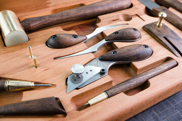 Exclusive handmade leather craft tools. Close up of different tanner tools on wooden box. Set of Different knifes from steel and wood. Black background.