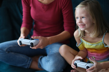 A little girl with a nanny sits on the couch plays a video gam