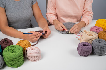 A woman teaches her friend needlework. Two women are crocheting a basket of cotton yarn.