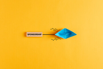 Paper boat pulls a wooden banner with the word sponsorship. Sponsoring, financial support or fundraising - obrazy, fototapety, plakaty
