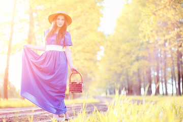 Young beautiful girl in dresses on nature. A girl in a hat walks in the park. Young woman on a picnic with a basket outside the city.